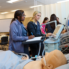 Respiratory students taking vitals with a practice medical mannequin.